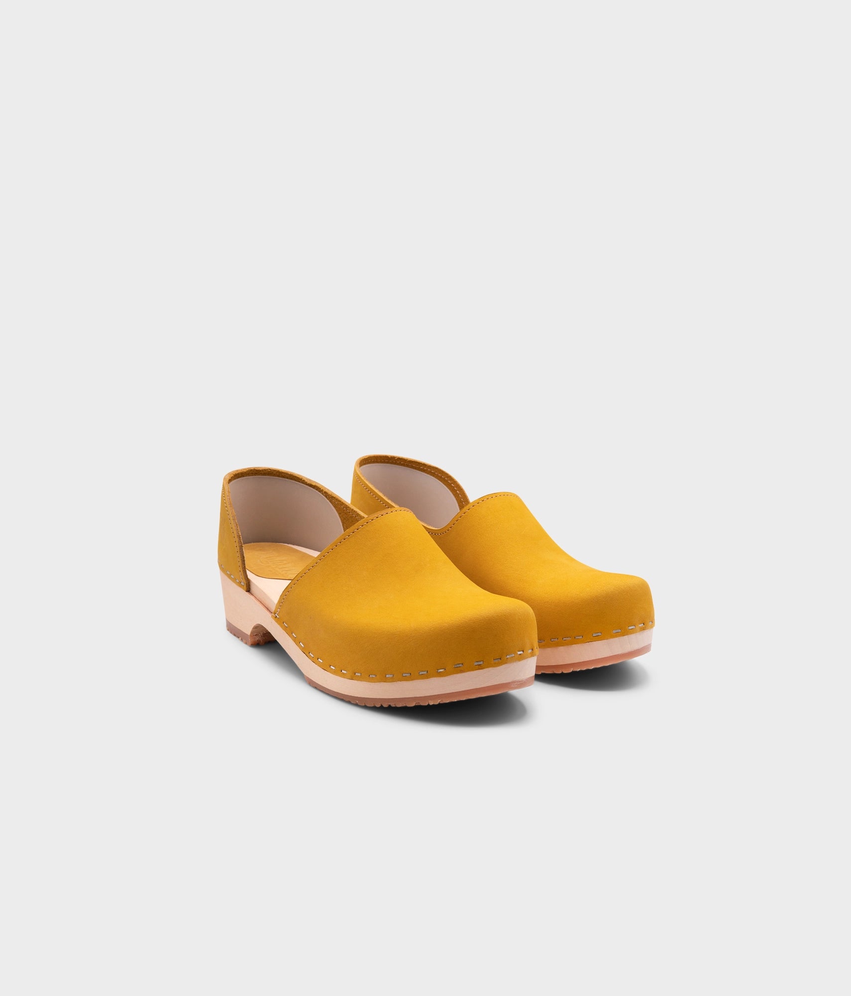 low heeled closed-back clogs in yellow nubuck leather stapled on a light wooden base