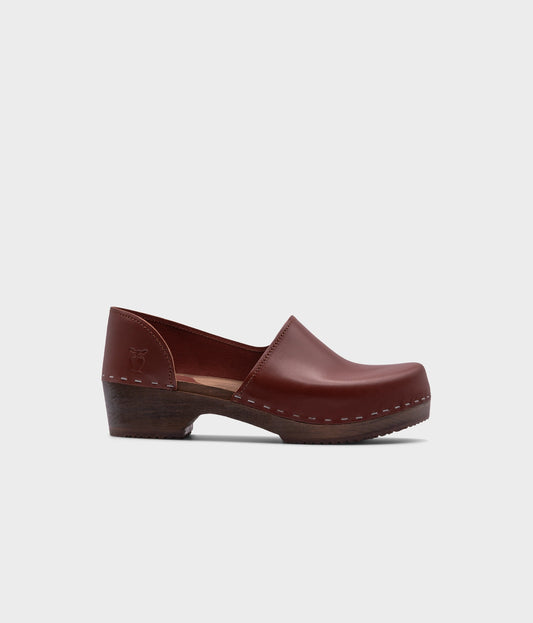 low heeled closed-back clogs in cognac vegetable tanned leather stapled on a dark wooden base