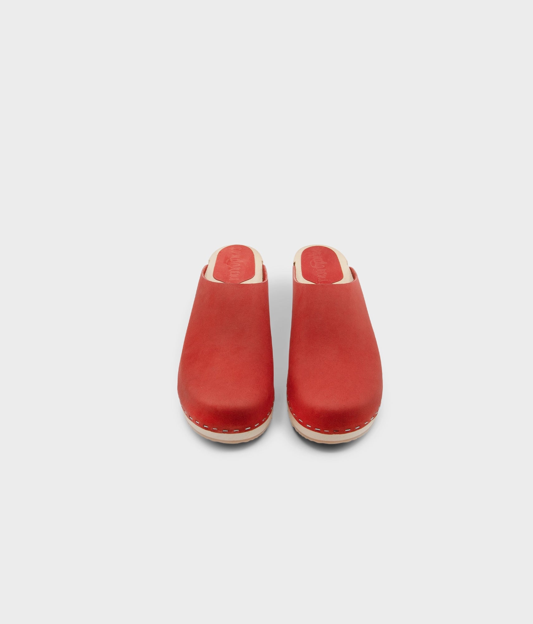 low heeled minimalistic clog mules in red nubuck leather stapled on a light wooden base