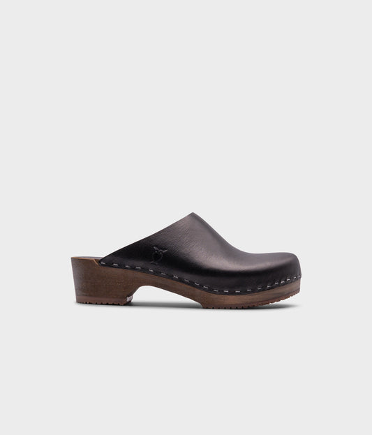 low heeled minimalistic clog mules in black vegetable tanned leather stapled on a dark wooden base