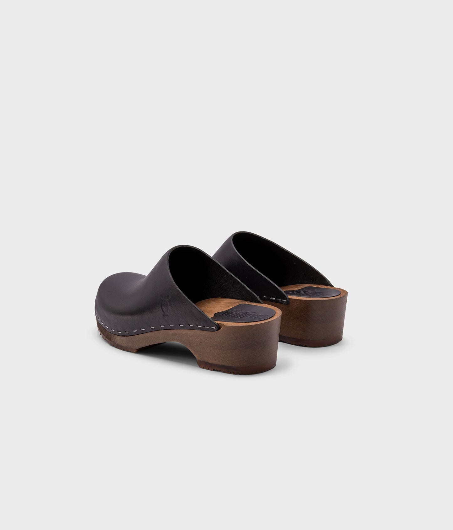 low heeled minimalistic clog mules in black vegetable tanned leather stapled on a dark wooden base