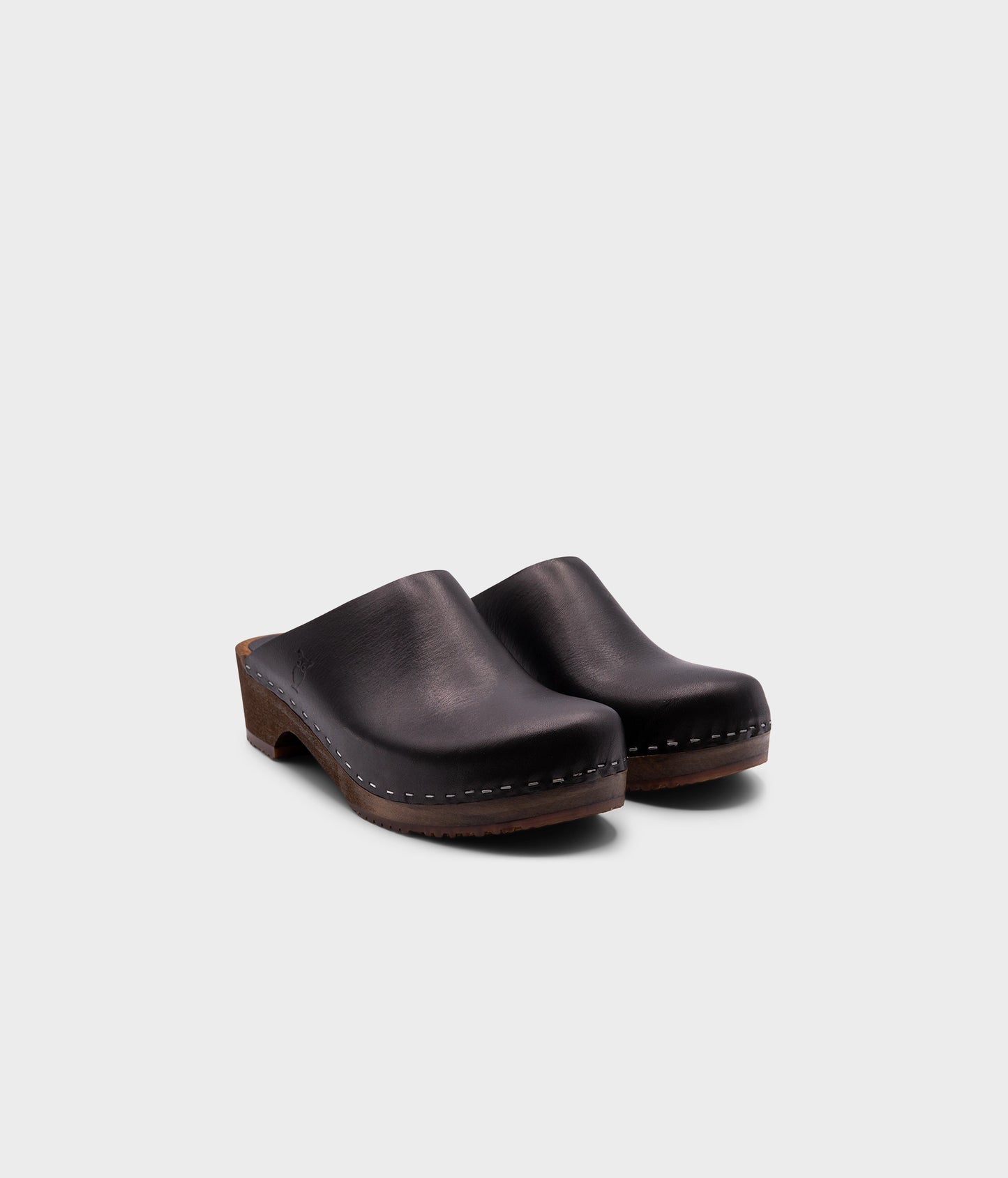 low heeled minimalistic clog mules in black vegetable tanned leather stapled on a dark wooden base