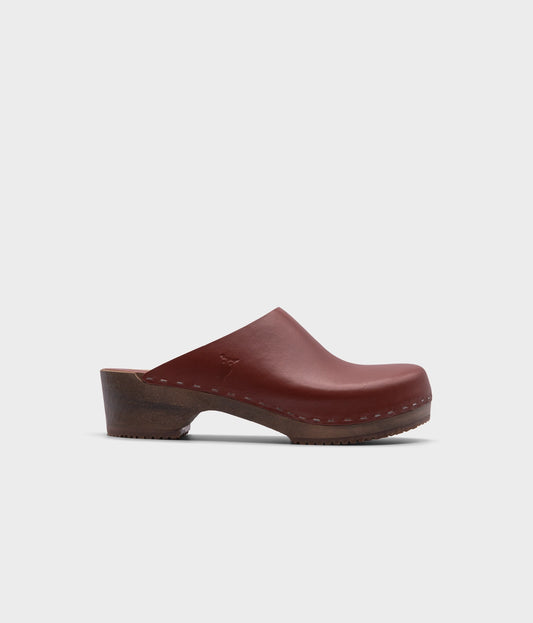 low heeled minimalistic clog mules in cognac vegetable tanned leather stapled on a dark wooden base