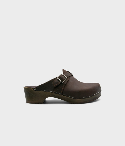 men's clog mule in brown nubuck leather stapled on a dark wooden base with a silver buckle on top