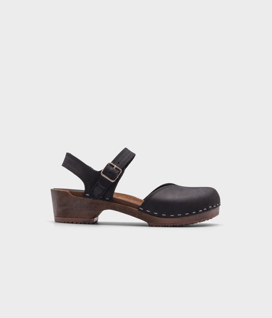 classic low heeled closed-toe sandal in black nubuck leather stapled on a dark wooden base