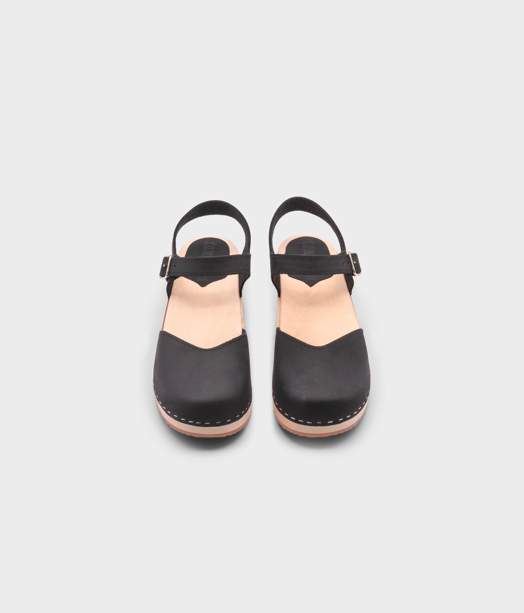 classic low heeled closed-toe sandal in black nubuck leather stapled on a light wooden base