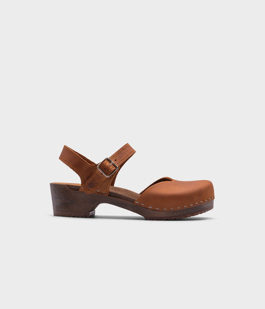 classic low heeled closed-toe sandal in light brown nubuck leather stapled on a dark wooden base
