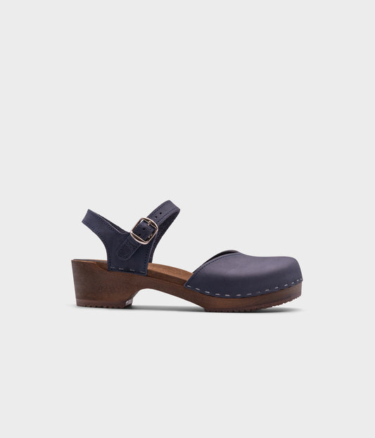 classic low heeled closed-toe sandal in navy blue nubuck leather stapled on a dark wooden base