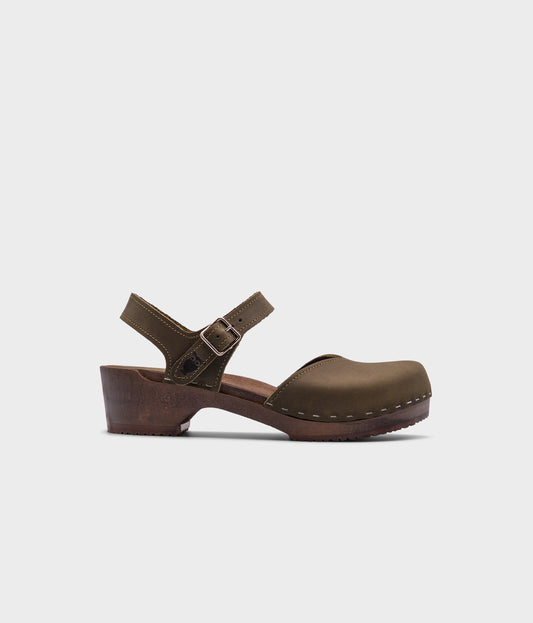 classic low heeled closed-toe sandal in olive green nubuck leather stapled on a dark wooden base