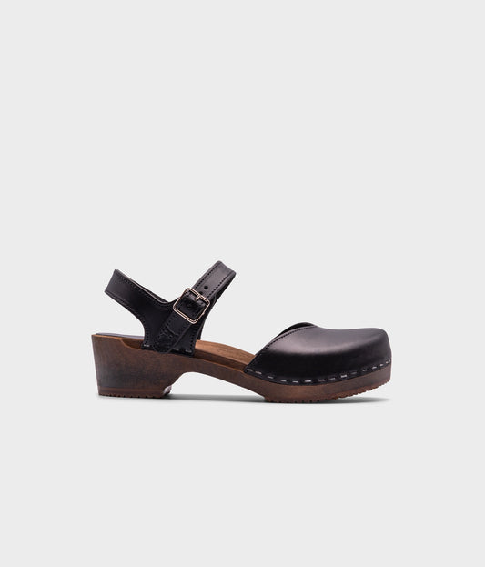 classic low heeled closed-toe sandal in black vegetable tanned leather stapled on a dark wooden base
