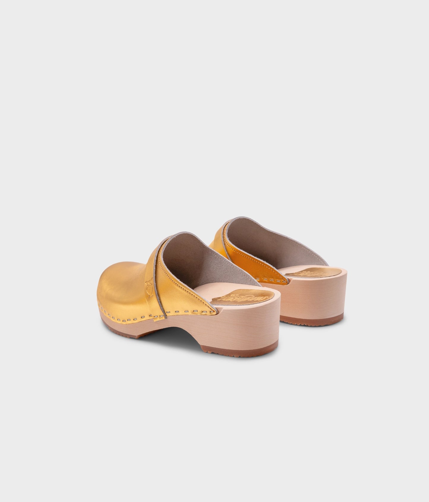 classic low heeled clog mule in metallic gold traditional leather stapled on a light wooden base with a leather strap