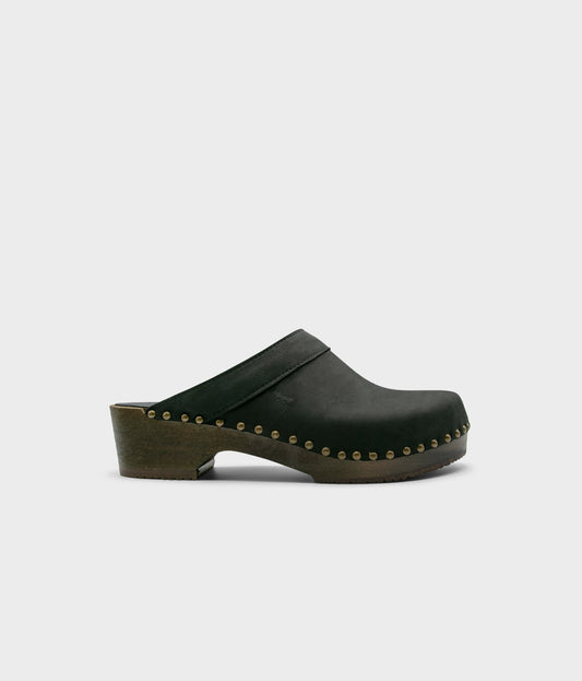 low heeled clog mules in black nubuck leather stapled on a dark wooden base with brass gold studs