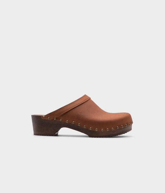 low heeled clog mules in dexter tan nubuck leather stapled on a dark wooden base with brass gold studs