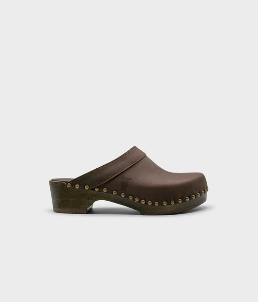 low heeled clog mules in dark brown nubuck leather stapled on a dark wooden base with brass gold studs