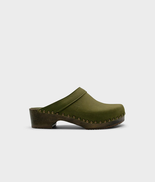 low heeled clog mules in olive green nubuck leather stapled on a dark wooden base with brass gold studs
