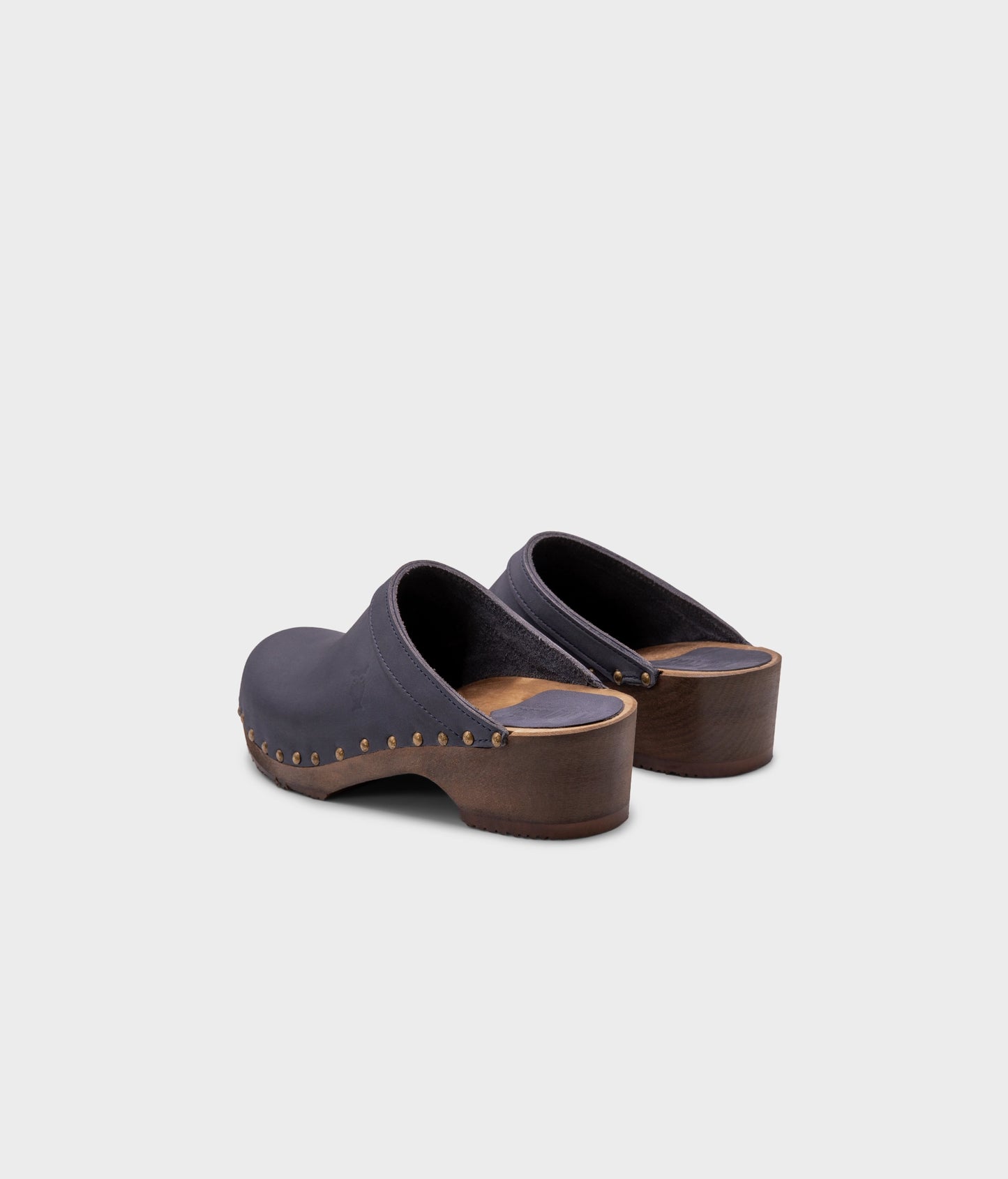 low heeled clog mules in navy nubuck leather stapled on a dark wooden base with brass gold studs