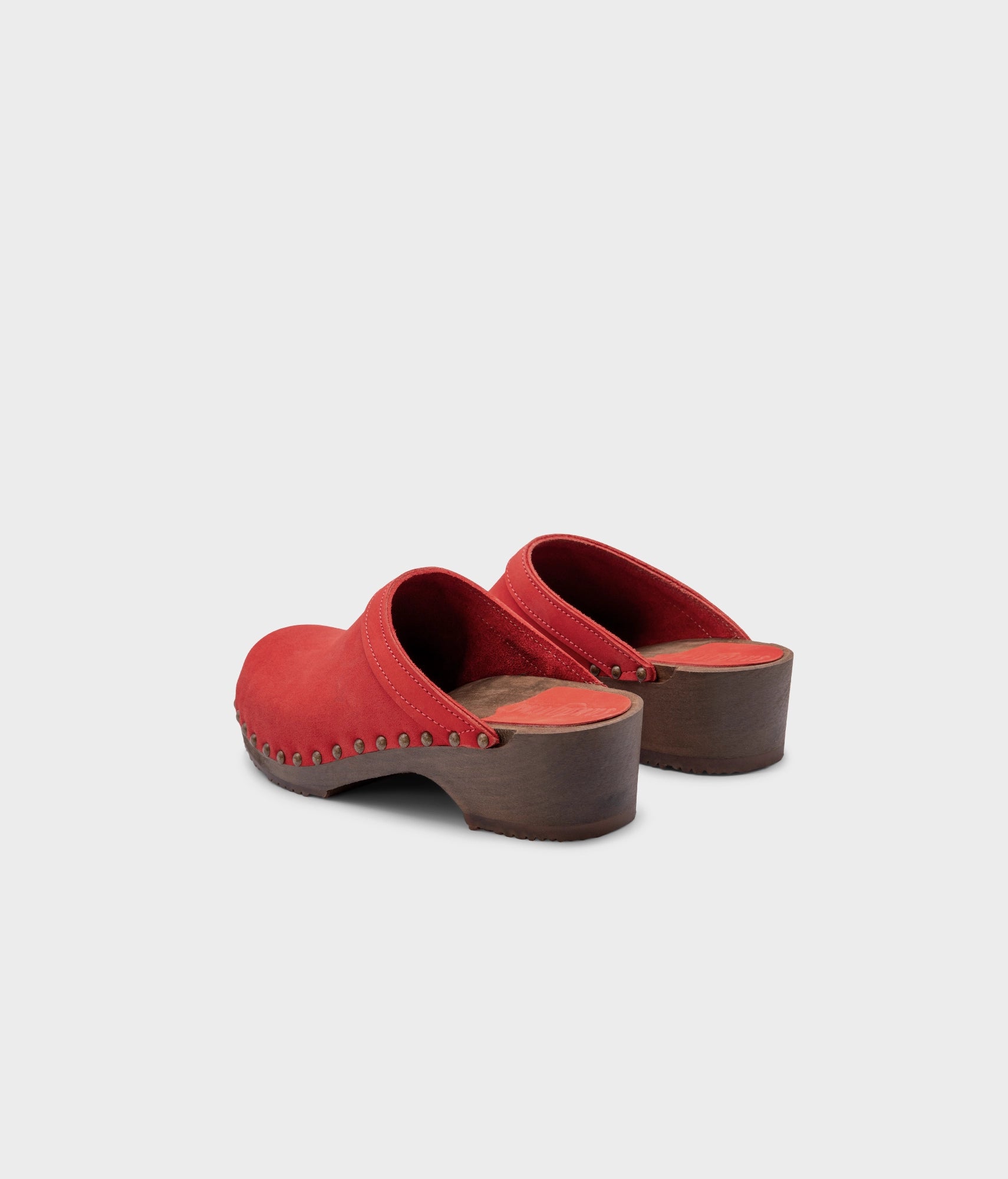 low heeled clog mules in red nubuck leather stapled on a dark wooden base with brass gold studs