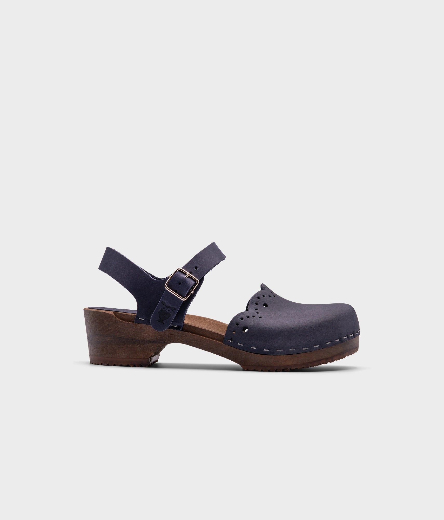 low heeled closed-toe clog sandals in navy blue nubuck leather with a wavy leather cutout stapled on a dark wooden base