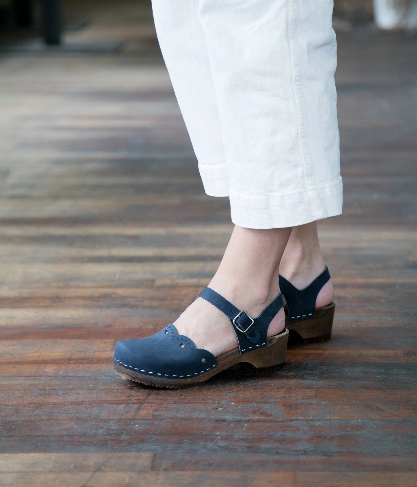 low heeled closed-toe clog sandals in navy blue nubuck leather with a wavy leather cutout stapled on a dark wooden base
