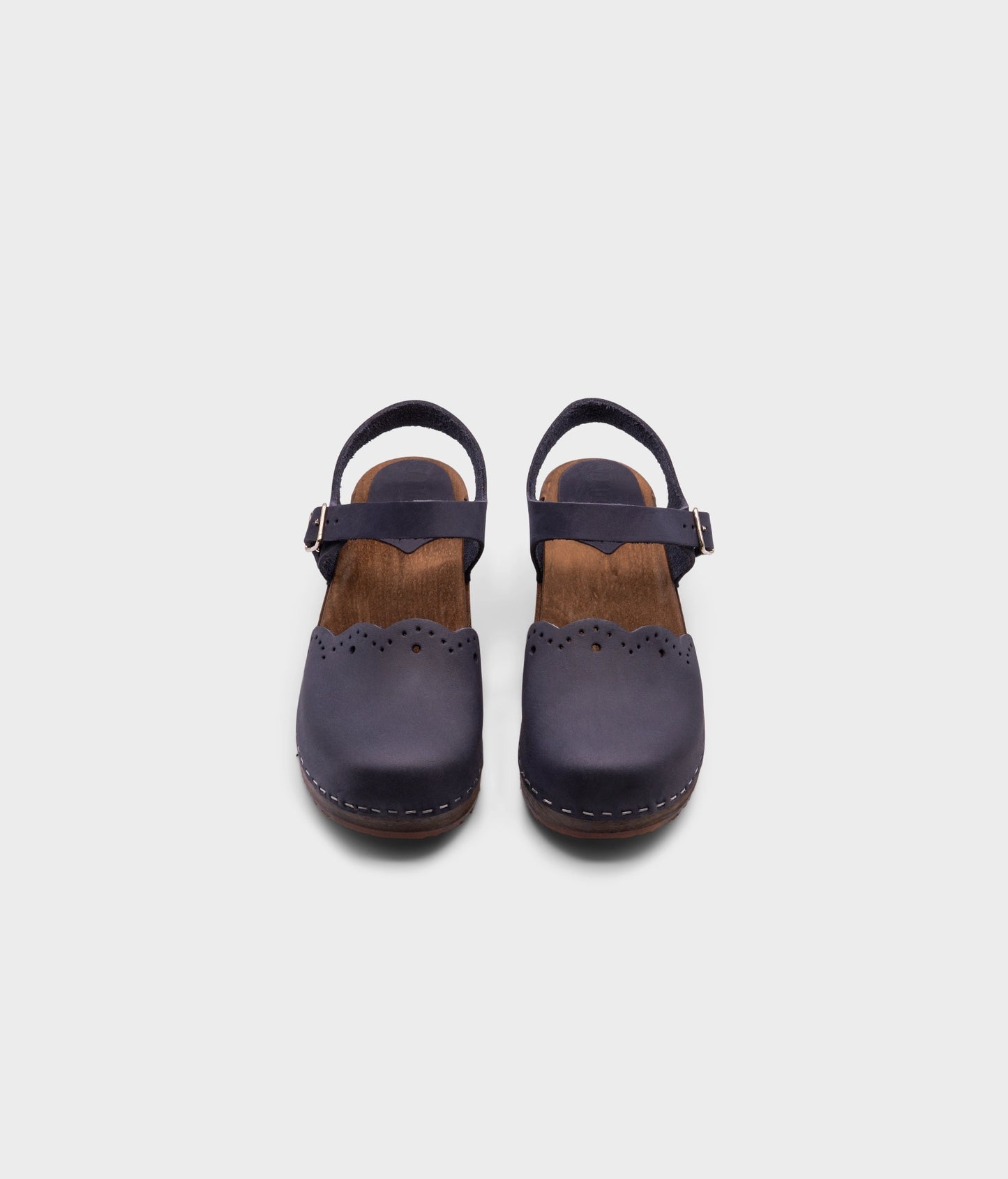 low heeled closed-toe clog sandals in navy blue nubuck leather with a wavy leather cutout stapled on a dark wooden base