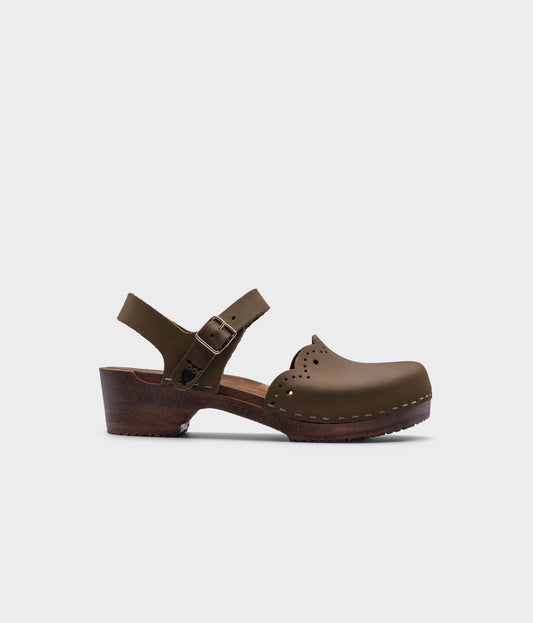 low heeled closed-toe clog sandals in olive green nubuck leather with a wavy leather cutout stapled on a dark wooden base