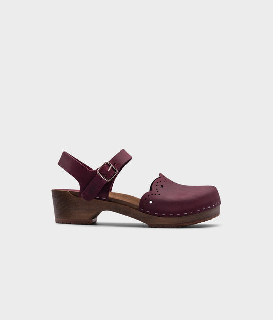 low heeled closed-toe clog sandals in plum purple nubuck leather with a wavy leather cutout stapled on a dark wooden base
