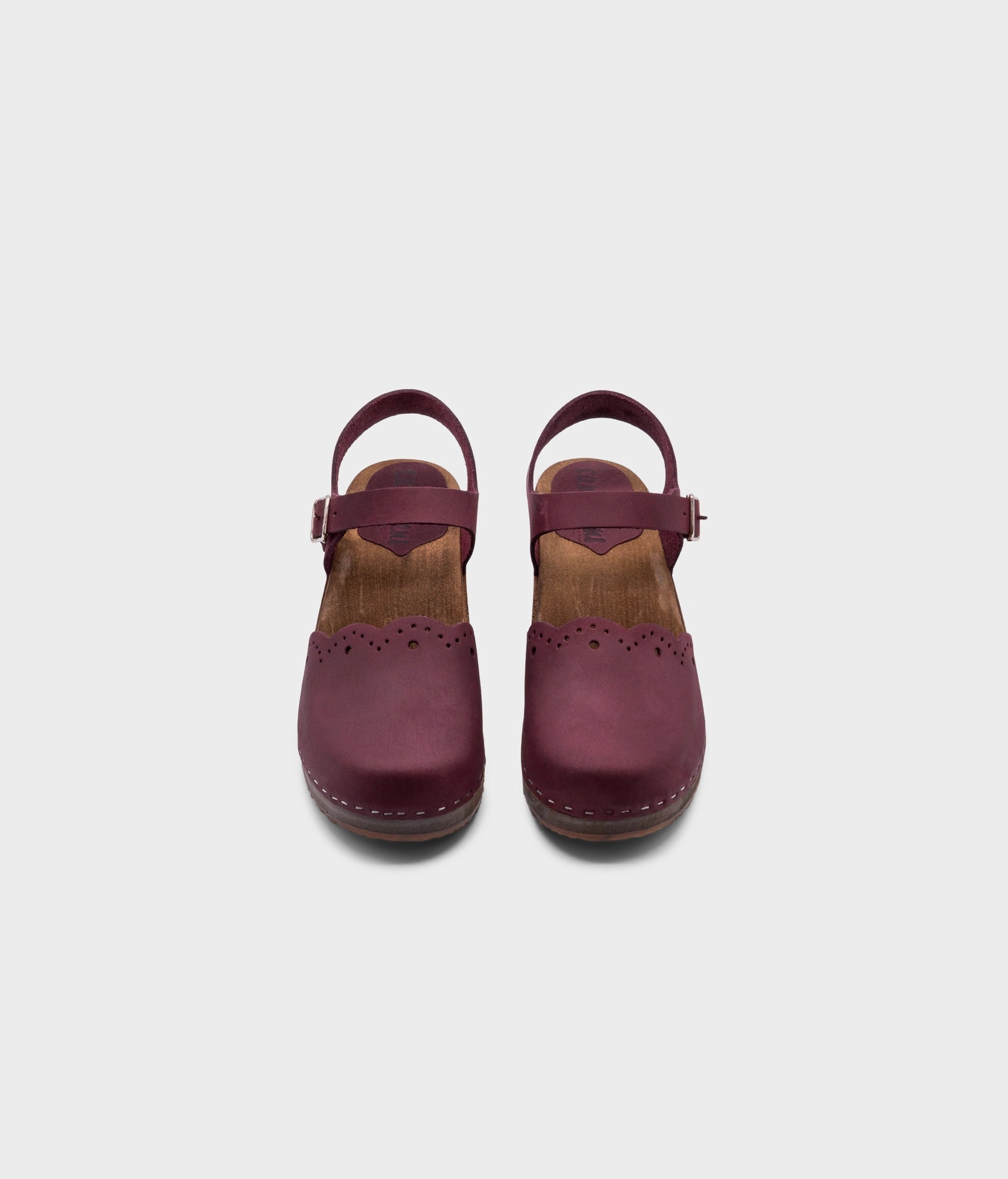 low heeled closed-toe clog sandals in plum purple nubuck leather with a wavy leather cutout stapled on a dark wooden base