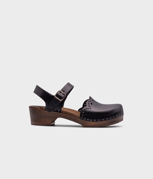 low heeled closed-toe clog sandals in black vegetable tanned leather with a wavy leather cutout stapled on a dark wooden base