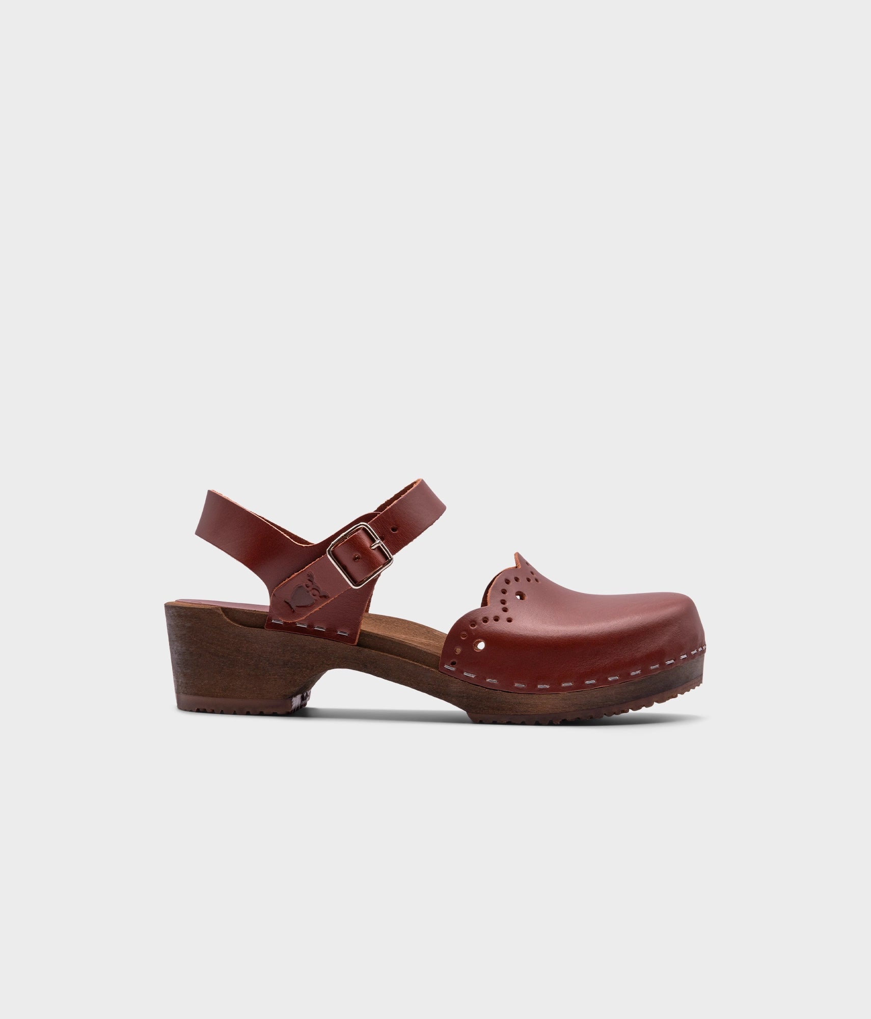 low heeled closed-toe clog sandals in cognac red vegetable tanned leather with a wavy leather cutout stapled on a dark wooden base