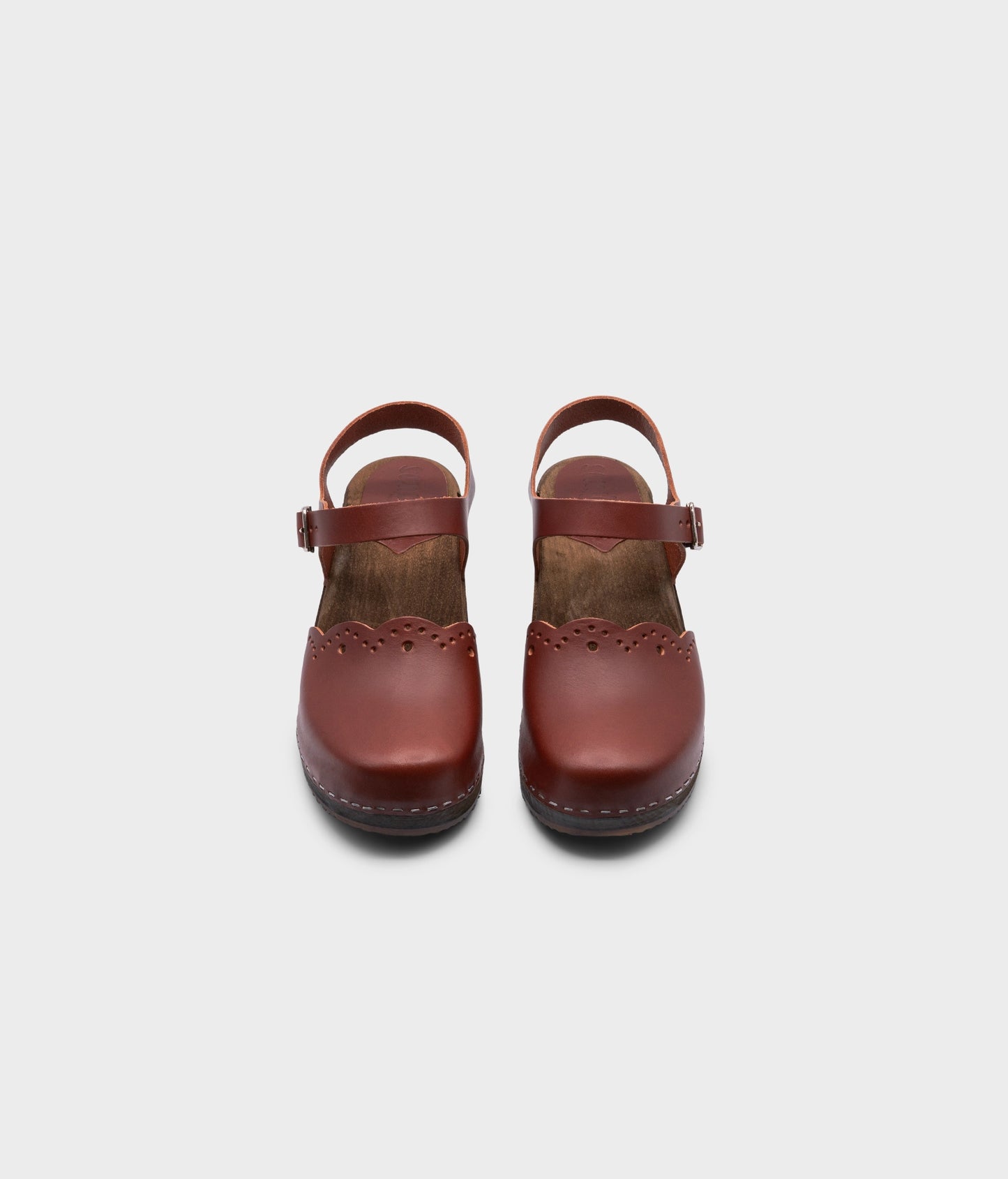 low heeled closed-toe clog sandals in cognac red vegetable tanned leather with a wavy leather cutout stapled on a dark wooden base