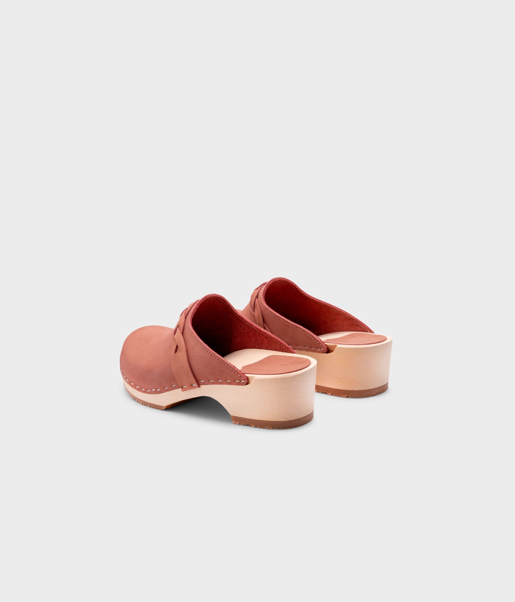 low heeled clog mules in blush pink nubuck leather with a braided strap stapled on a light wooden base