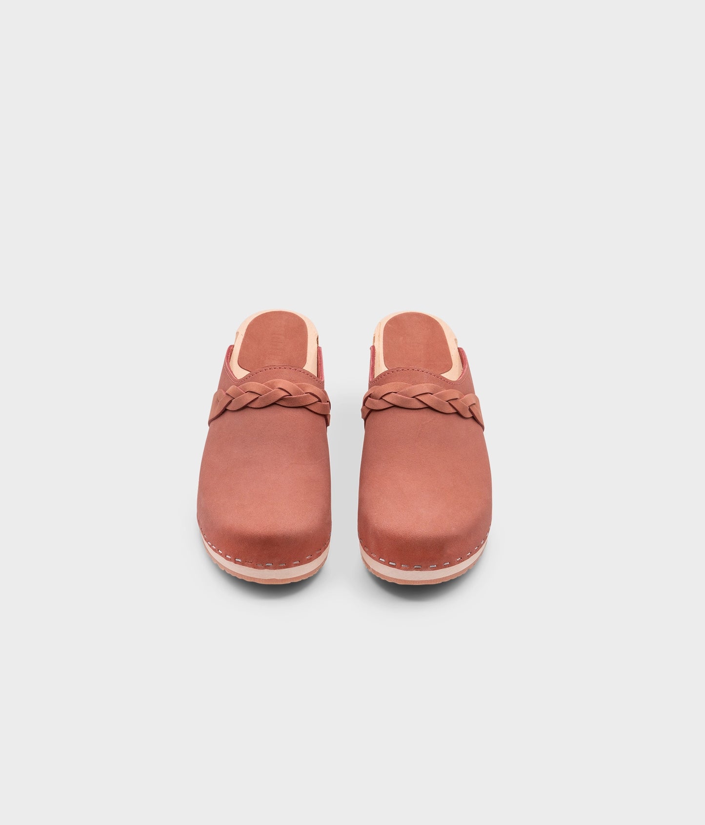 low heeled clog mules in blush pink nubuck leather with a braided strap stapled on a light wooden base