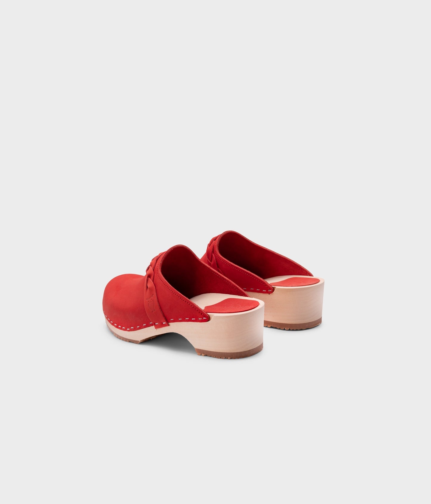 low heeled clog mules in red nubuck leather with a braided strap stapled on a light wooden base