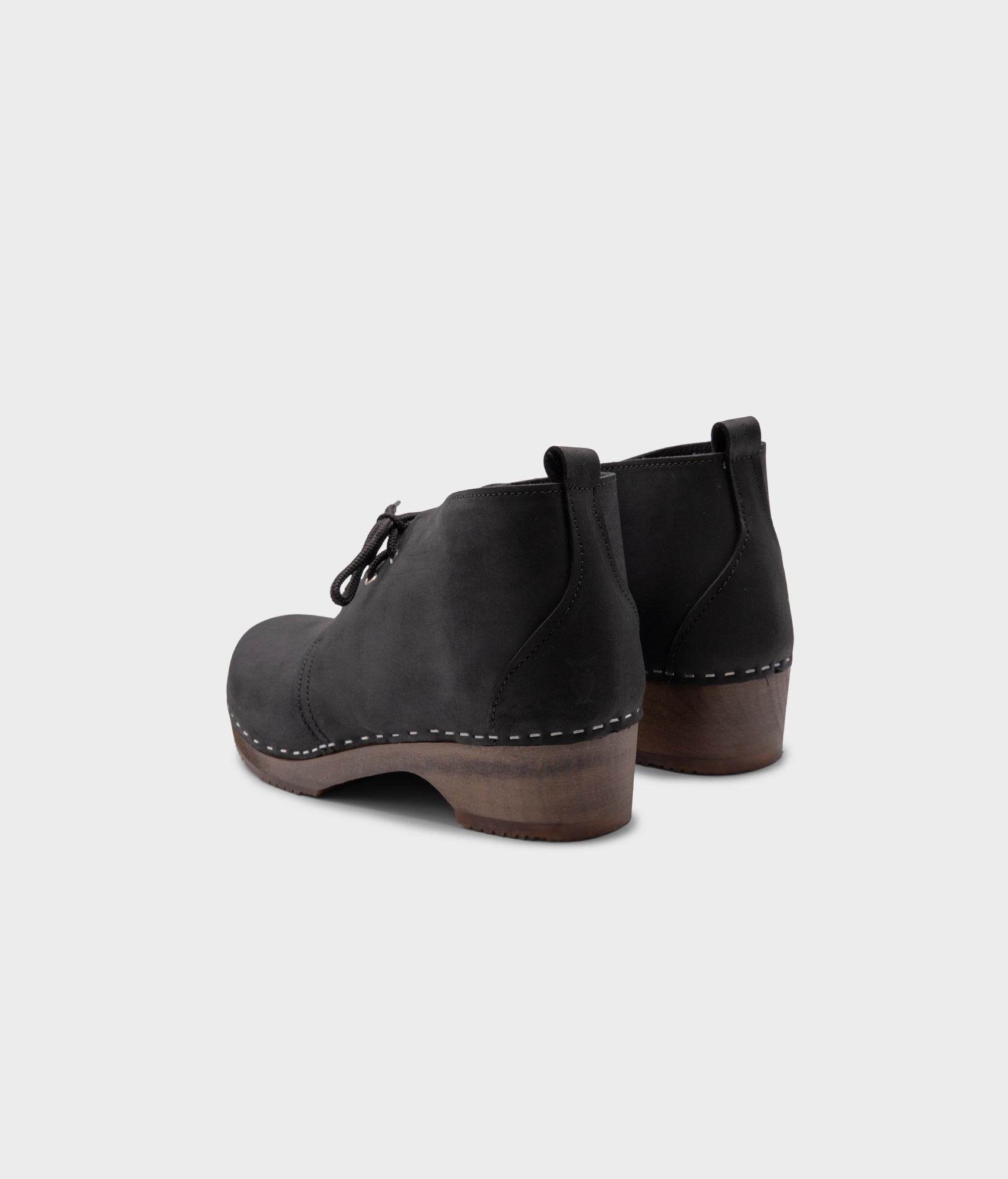 low heeled mens chukka clog boots in black nubuck leather stapled on a dark wooden base with black laces