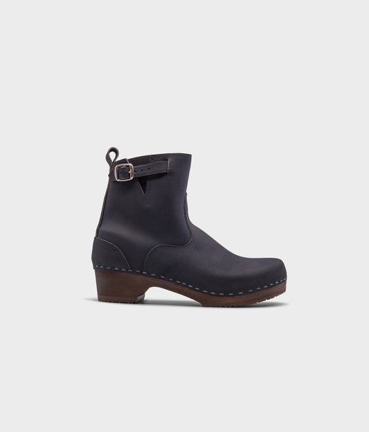 low heeled clog boots in navy blue nubuck leather with a mid-shaft and silver buckle, stapled on a dark wooden base