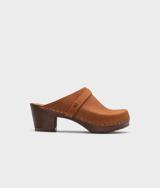 classic high heeled clog mule in light brown nubuck leather stapled on a dark wooden base with a leather strap