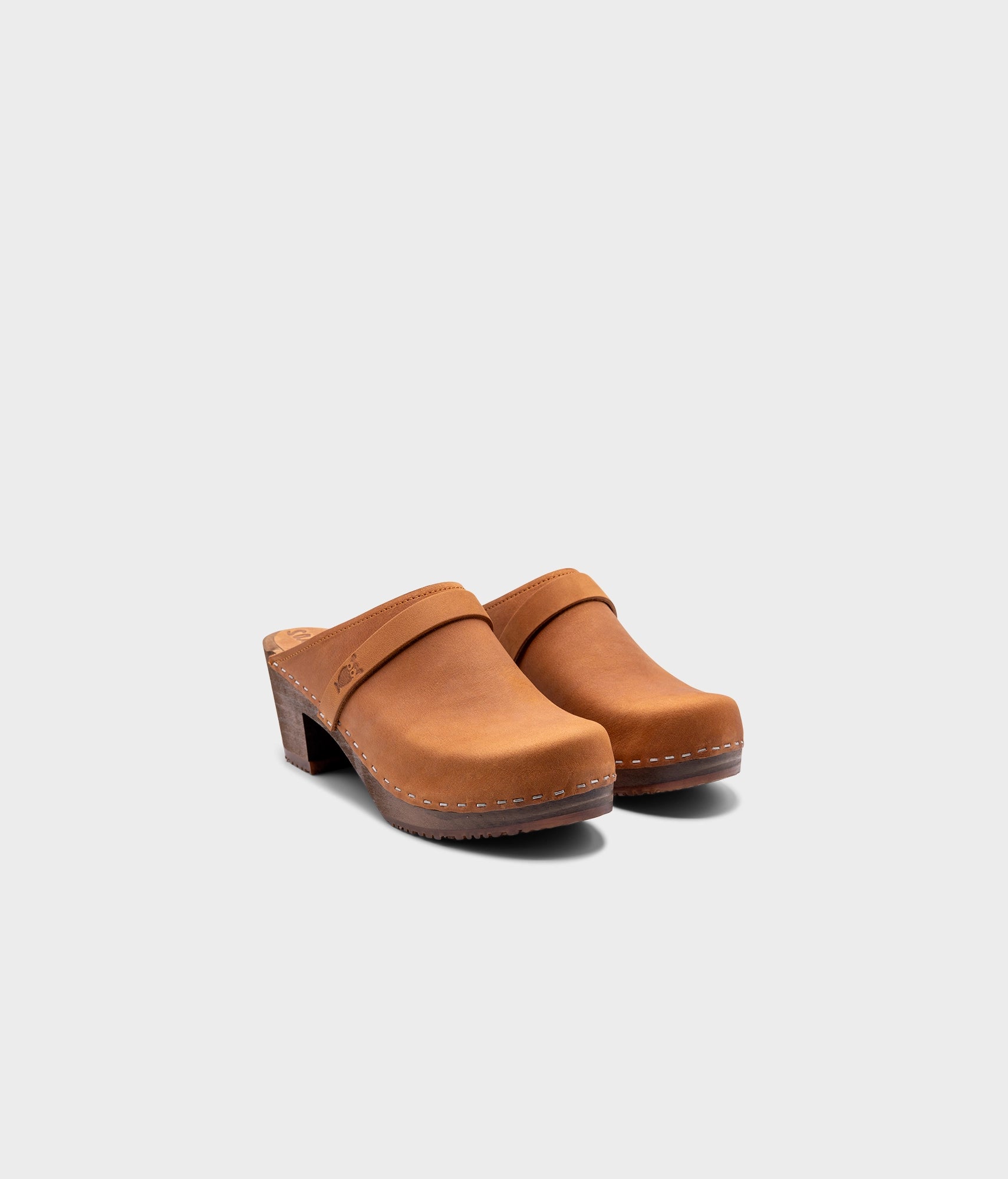 classic high heeled clog mule in light brown nubuck leather stapled on a dark wooden base with a leather strap