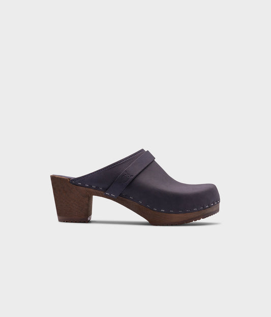 classic high heeled clog mule in navy blue nubuck leather stapled on a dark wooden base with a leather strap