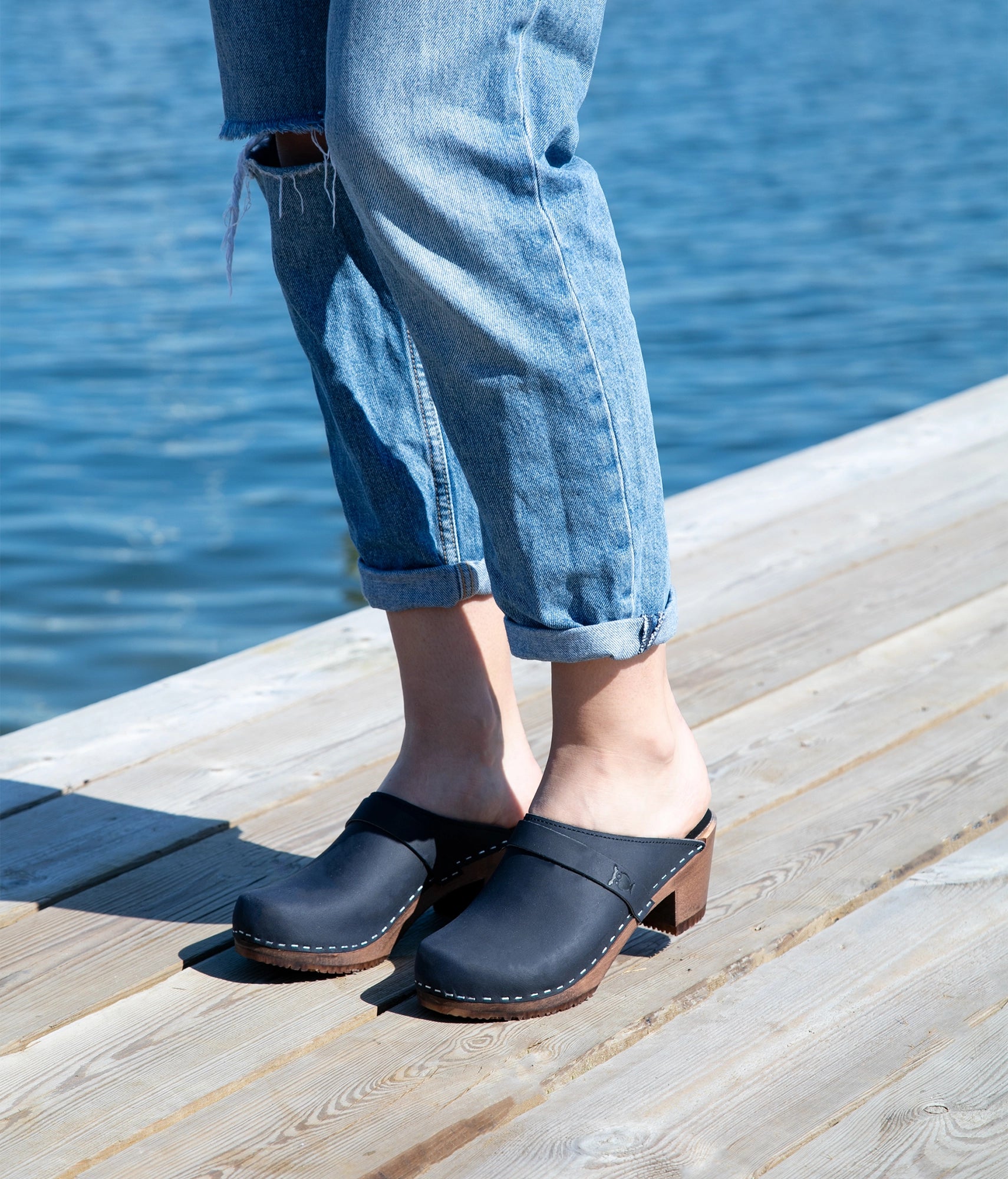 classic high heeled clog mule in navy blue nubuck leather stapled on a dark wooden base with a leather strap