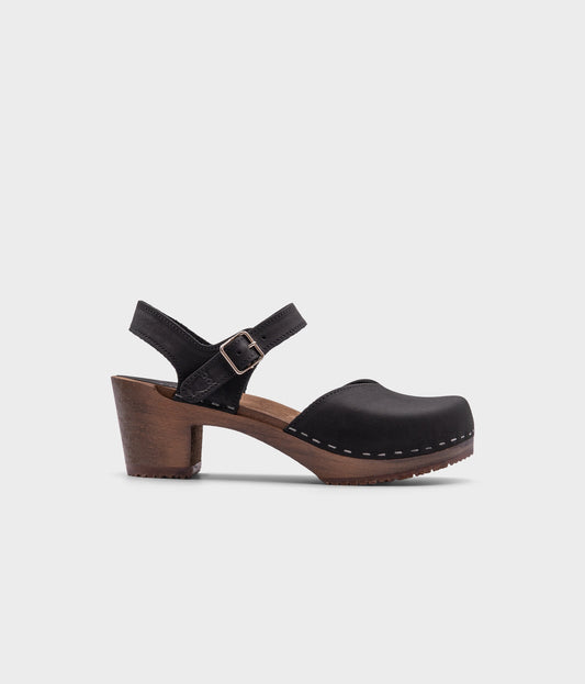 high heeled closed-toe clog sandal in black nubuck leather stapled on a dark wooden base