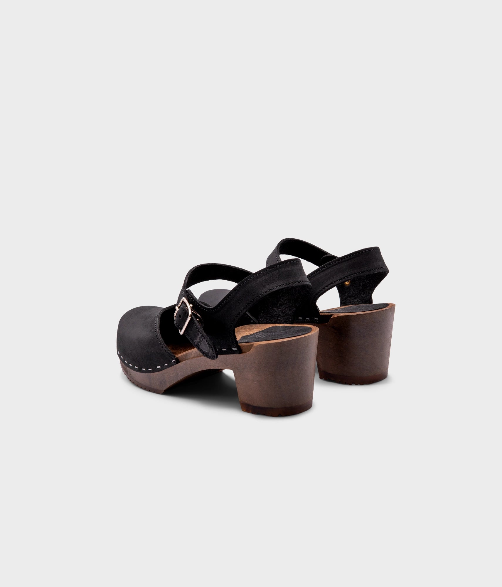 high heeled closed-toe clog sandal in black nubuck leather stapled on a dark wooden base