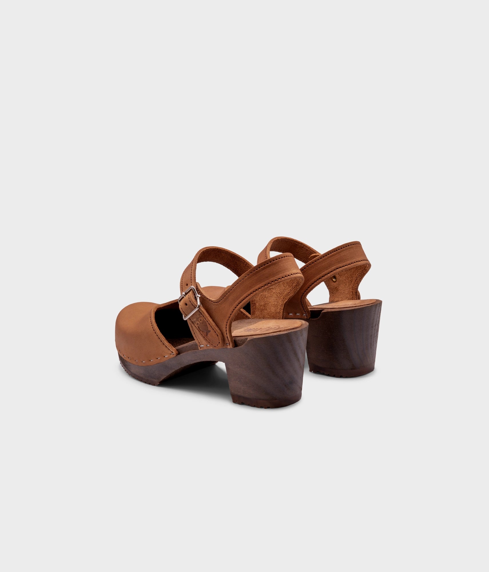 high heeled closed-toe clog sandal in light brown nubuck leather stapled on a dark wooden base