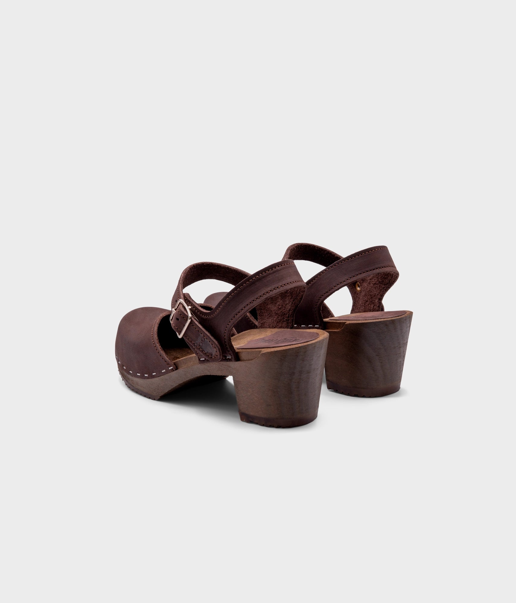 high heeled closed-toe clog sandal in dark brown nubuck leather stapled on a dark wooden base