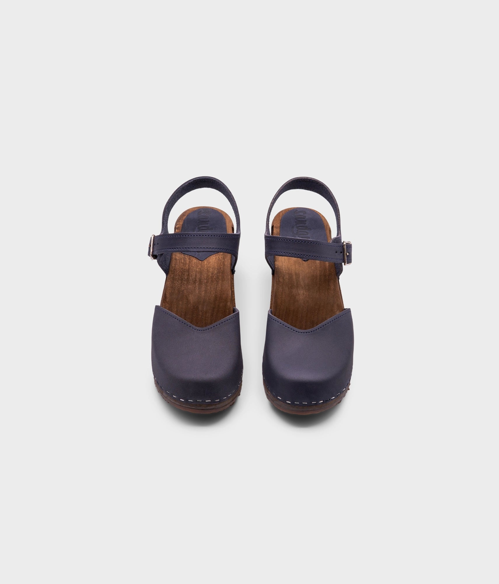 high heeled closed-toe clog sandal in navy blue nubuck leather stapled on a dark wooden base