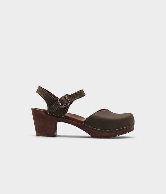 high heeled closed-toe clog sandal in olive green nubuck leather stapled on a dark wooden base
