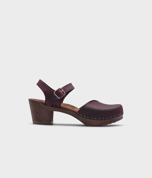 high heeled closed-toe clog sandal in purple plum nubuck leather stapled on a dark wooden base