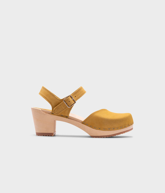 high-heeled clog sandals with a closed toe in yellow leather stapled on a light wooden base