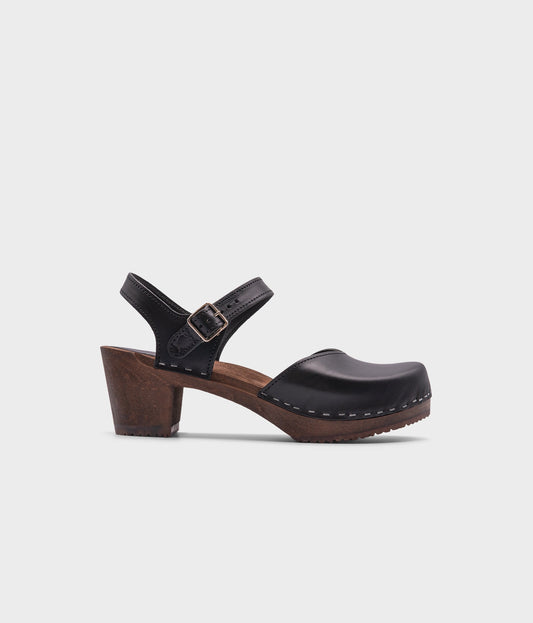 high heeled closed-toe clog sandal in black vegetable tanned leather stapled on a dark wooden base