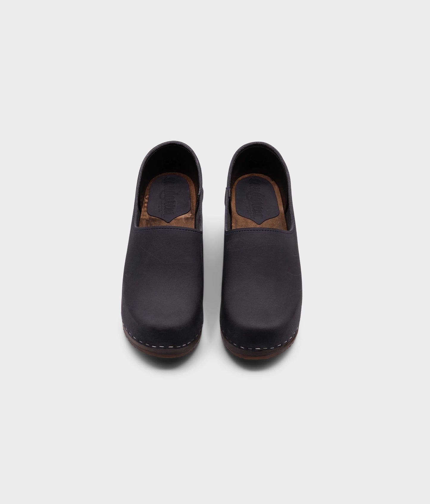 high heeled closed-back clogs in navy blue nubuck leather stapled on a dark wooden base
