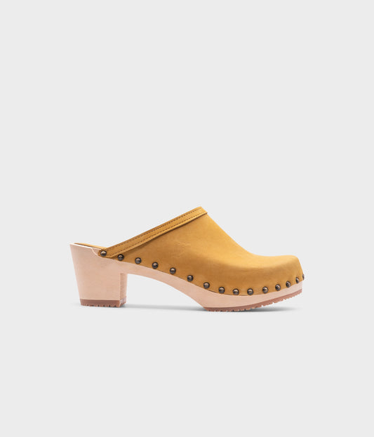 high heeled clog mules in yellow nubuck leather stapled on a light wooden base with brass gold studs